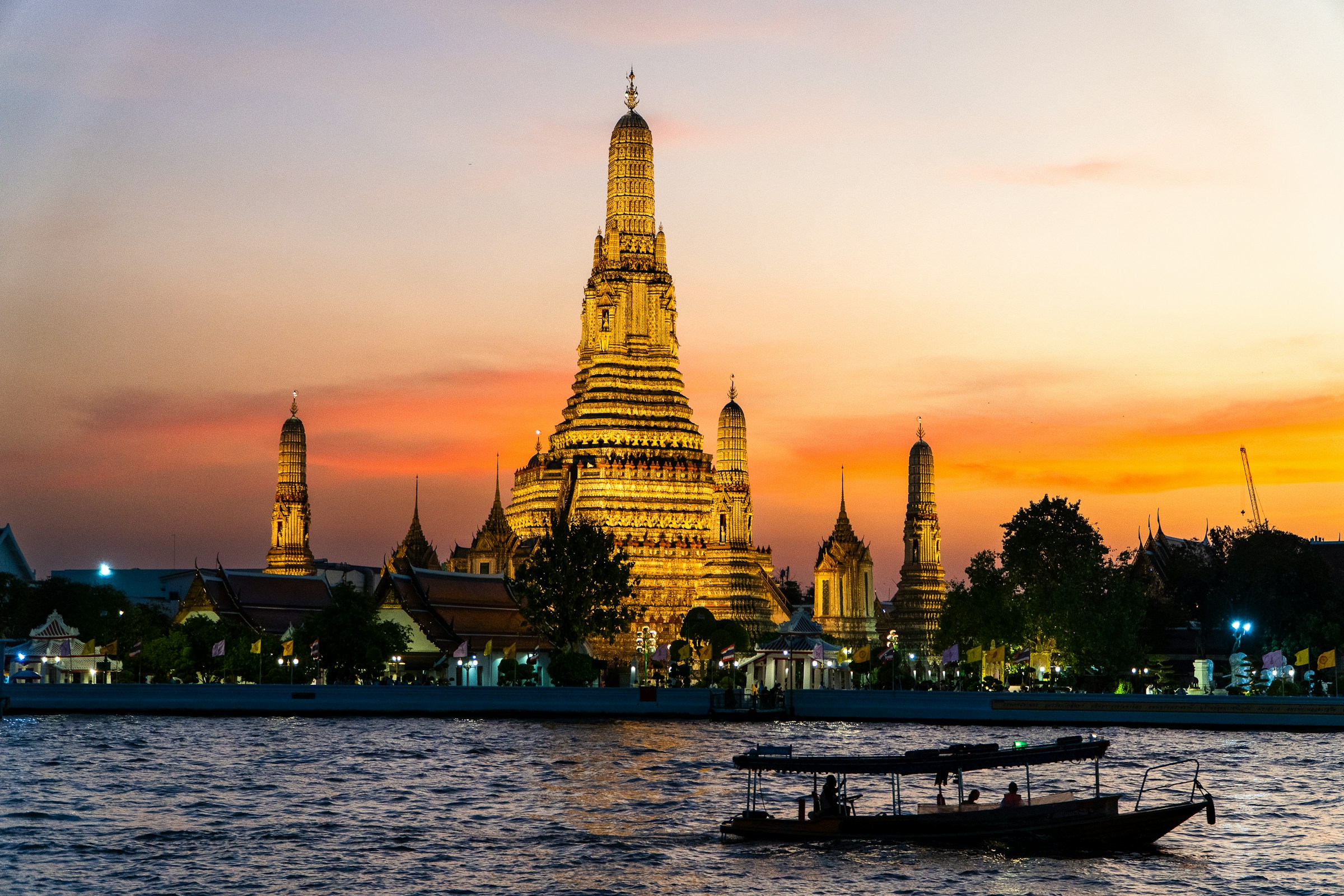 Wat Arun temple in Bangkok at sunset with traditional longtail boat on Chao Phraya River